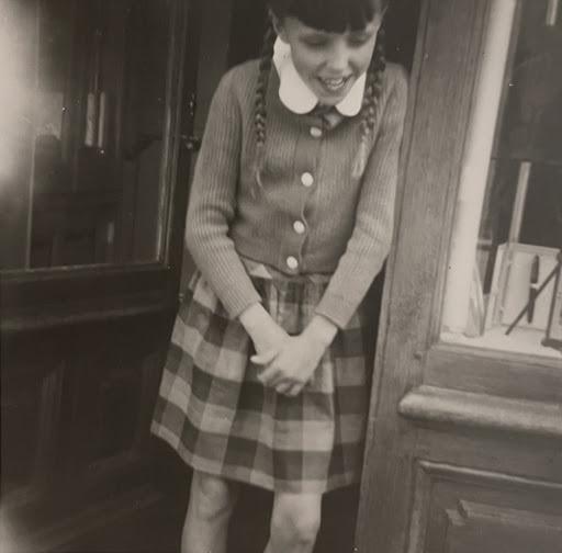 A schoolgirl in a cardigan and checked skirt laughing in a doorway