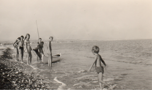 Children paddling from a pebble beach beside a small boat
