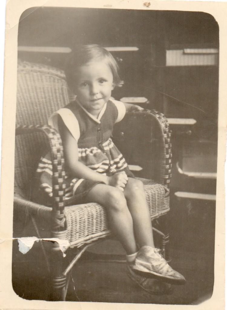 A young girl in a striped dress sitting in a wicker armchair